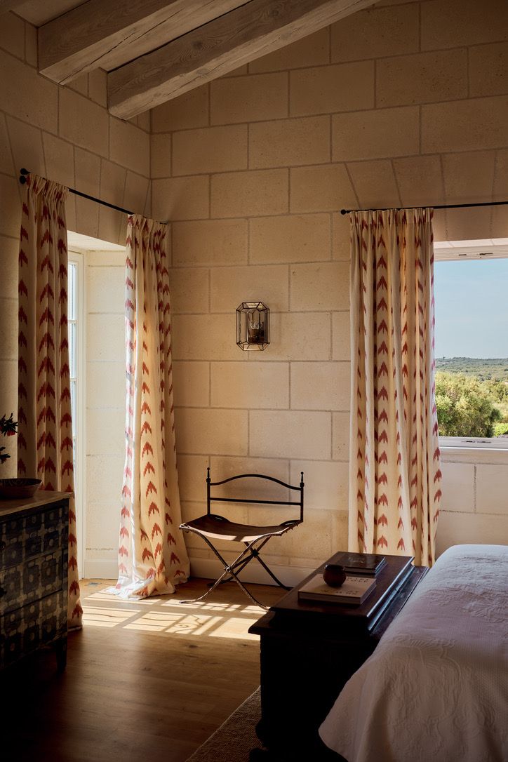 A bedroom corner in stone, with ikat curtains and countryside beyond