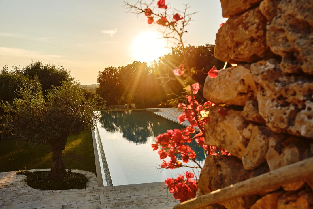 The sun setting over the pool beside the stone wall and bougainvillea